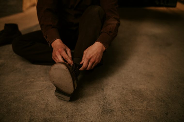 Hands tying a boot on a concrete floor